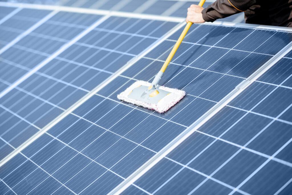 Cleaning solar panels with a mop and pole on a rooftop installation.