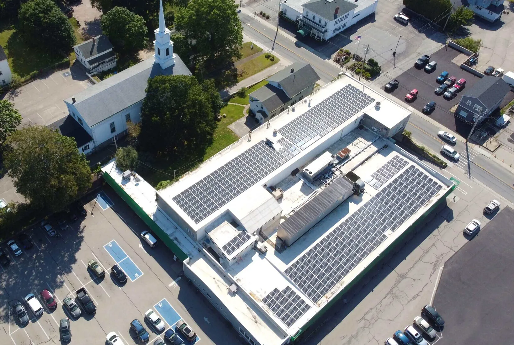 Aerial view of commercial building with solar panels and church in the background.