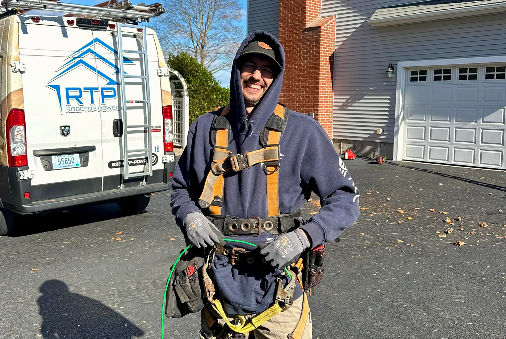 Rooftop Power technician installing solar panels on a residential roof, with company van and equipment.
