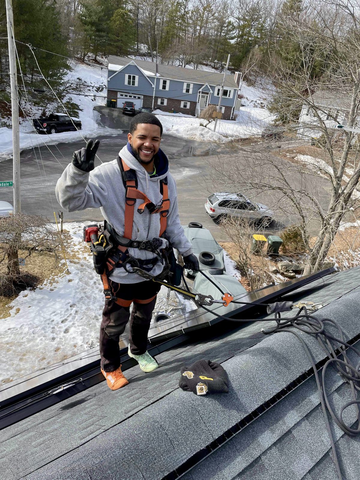 Rooftop Power crew member in fall protection gear on snow-covered roof with solar panels and soft-tool equipment.