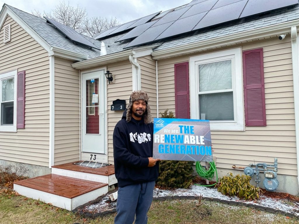 Rooftop Power customer in Warwick, Rhode Island, with solar panels and "The Renewable Generation" sign.