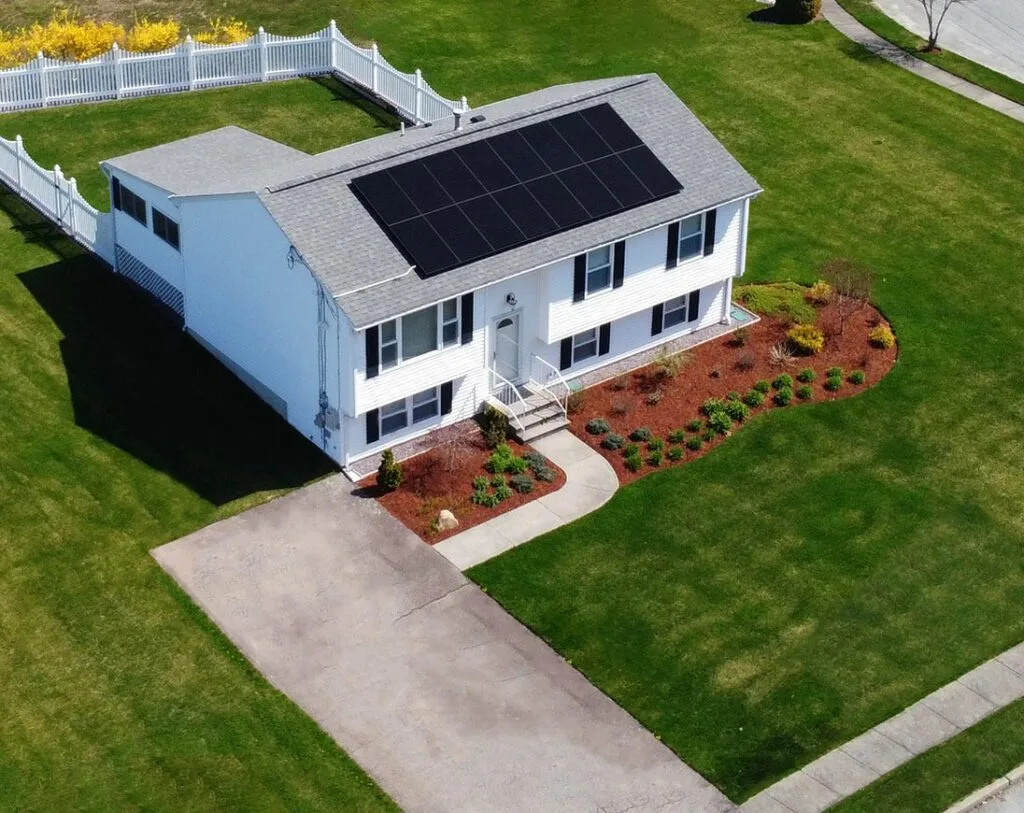 Aerial view of an all-black solar array installed by Rooftop Power on a white raised ranch home with a fenced yard.